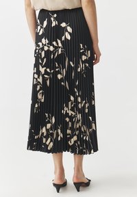 Gonna midi plissettata nera con un motivo floreale crema, dotata di una vita aderente e una silhouette fluida. Accessorio: scarpe a punta.