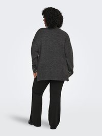 Dark gray knitted sweater with a loose fit, ribbed cuffs, and open knit detail on sleeves. Paired with black, wide-leg pants.