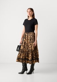 Top corto nero a maniche corte abbinato a una gonna lunga maxi con stampa leopardata marrone, caratterizzata da volant e una fascia nera di accento, completata da stivali neri alti fino al ginocchio.