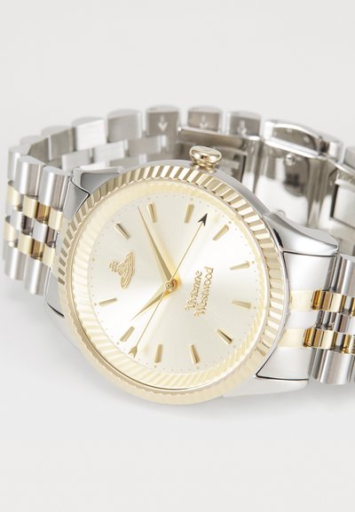 Roostevabast terasest kell, millel on kaheliitrine hõbedane ja kuldne rihm. Omab kuldset kellaplaati, ribakujulist äärist ja tunni näitajat.