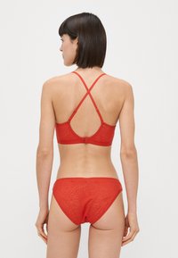 Piros bikiniszett, amelynek textúrázott melltartója keresztezett pántokkal és hozzáillő alsórésszel rendelkezik. Simább anyagból készült, finom mintázattal.
