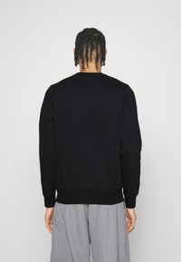 Svart sweatshirt med rund hals, långärmar och ribbade mudd. Slät textur och avslappnad passform, bärs med grå byxor.