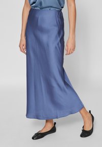 Jupe maxi en satin bleu avec une texture lisse, dotée d'une taille ajustée et d'un design fluide, associée à des chaussures plates noires.