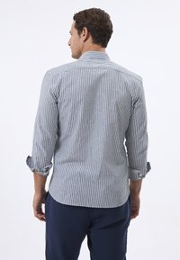 Camisa de rayas en algodón azul y blanco con mangas enrolladas, que presenta un cuello clásico y un dobladillo curvado, con costuras y botones visibles.