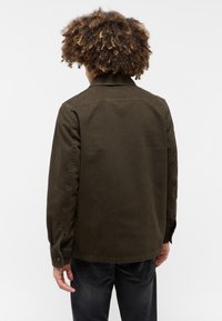 Giacca verde oliva con colletto a bottoni, maniche lunghe e dettaglio sulla parte posteriore. Realizzata in tessuto testurizzato, con una vestibilità rilassata.