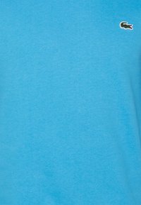 Camiseta de algodón azul con una textura suave y un pequeño logotipo de cocodrilo verde en el lado izquierdo del pecho. Dobladillo recto, mangas cortas.