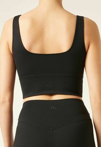 Espalda de una mujer que lleva una camiseta negra de corte corto y leggings de cintura alta con pequeños logotipos "clz" centrados en ambas prendas.
