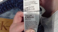 Étiquette en jean en denim avec instructions de lavage. Étiquette en tissu blanc avec des symboles pour le lavage, le séchage et le repassage. Comprend du texte en anglais et multilingue.