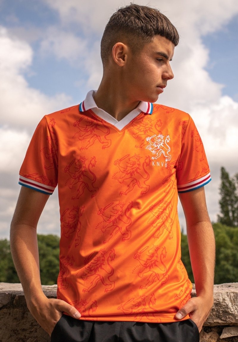 Oranje voetbalshirt met een leeuwenpatroon, voorzien van een witte kraag en blauwe strepen op de mouwen. Lichtgewicht, atletische pasvorm.