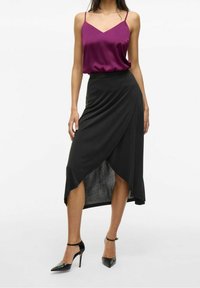 Jupe noire enveloppante avec un ourlet asymétrique et une texture lisse, associée à un caraco en satin violet à fines bretelles. Chaussures à talons hauts noires.