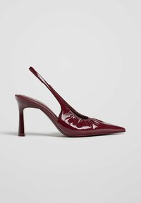 Escarpin slingback en cuir verni bordeaux brillant, talon haut, bout pointu et détail froncé sur le dessus, sur fond uni.