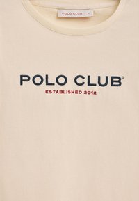 Cremfarbene Baumwoll-T-Shirt mit Rundhalsausschnitt. Mit gesticktem Schriftzug "POLO CLUB" in Marineblau und "ESTABLISHED 2012" in roter Schrift.