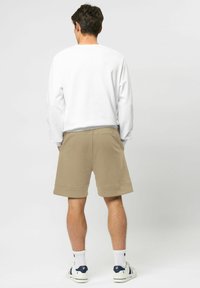 Vit långärmad skjorta, beige shorts och vita strumpor tillsammans med sneakers. Mjukt tyg med en avslappnad passform, synlig sömnad på shorts.