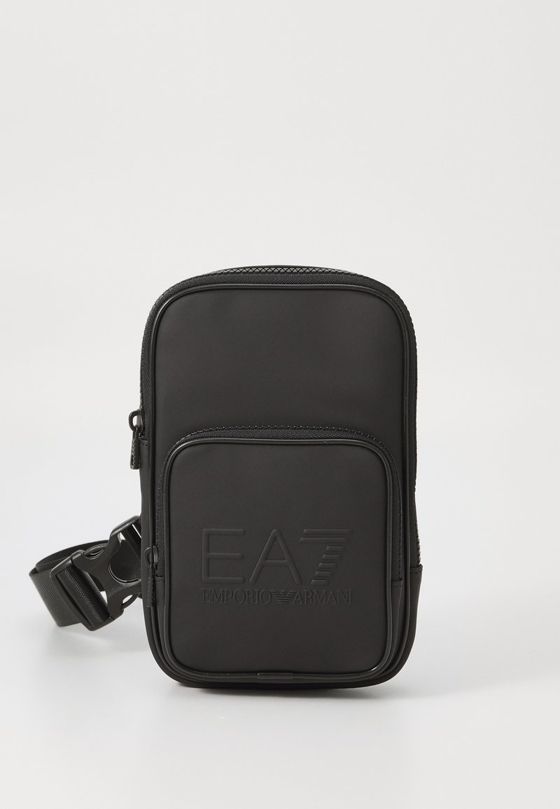 Sac à épaule multifonction noir en matériau synthétique lisse. Dispose d'une poche zippée à l'avant et du logo EA7 en relief. Sangle réglable incluse.