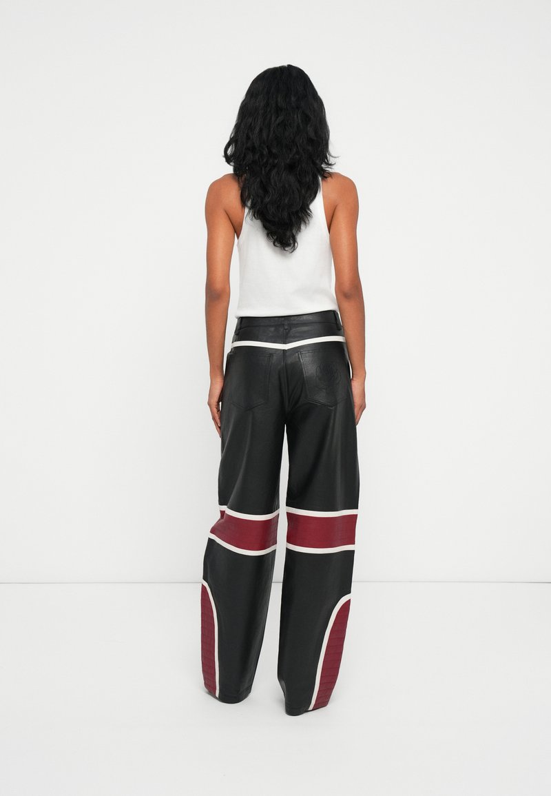 Pantalones de cuero negros con piernas anchas, que presentan acentos rojos y blancos en un patrón geométrico, y detalles en los bolsillos traseros.