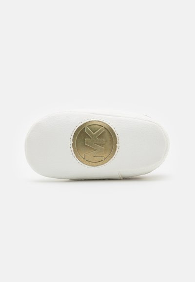 Adidași albi cu un superior din piele texturată, vârf rotund și un logo rotund auriu proeminent pe lateral. Talpa pare flexibilă și plată.