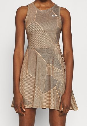 Femme portant une robe sans manches beige et noire à motif géométrique, jupe évasée et petit logo blanc sur la poitrine.