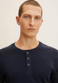 Camisa henley de manga larga en color marino, fabricada en tejido suave, con tres botones, cuello tipo crew y discretos detalles de costura en los hombros.