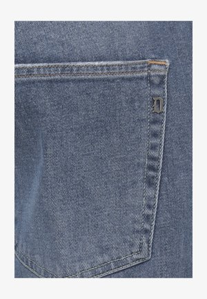 Tasca posteriore di jeans di denim blu con cuciture visibili e una piccola lettera metallica "D" attaccata sul lato destro.