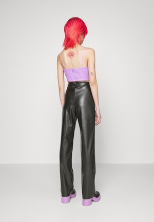 Personne aux cheveux rose vif, vue de dos, portant un crop top violet, un pantalon en cuir noir et des chaussures à plateforme violettes.