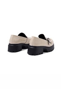 Mocassini in pelle verniciata beige con punta rotonda, tacco in gomma nera chunky e dettagli in metallo argentato nella parte anteriore.