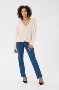 Ljusrosa stickad kavaj med V-ringning, enkel knappstängning och ribbade ärmslut. Paret med blå raka jeans och svarta klackar.