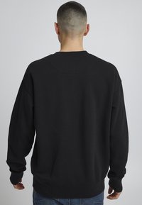 Black sweatshirt, crew neck, relaxed fit, long sleeves, ribbed cuffs and hem, soft texture, plain without patterns or logos.