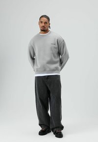 Grijze trui met geribbelde manchetten en zoom, gecombineerd met loszittende zwarte jeans en zwarte schoenen met roze veters. Eenvoudig, minimalistisch ontwerp.