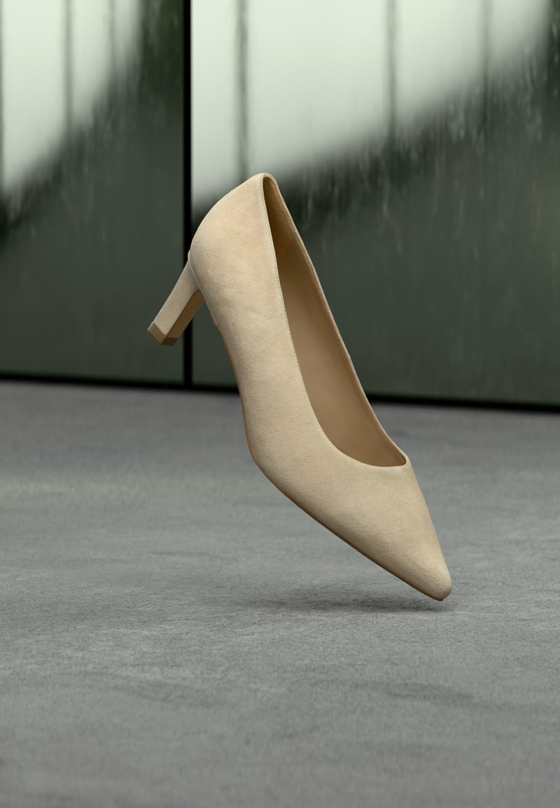 Escarpin beige en daim à talon haut avec un bout pointu et un talon bloc modeste, présenté sur un fond gris texturé.
