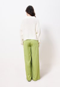 Weißer Strickpullover mit offener Maschenstruktur und verkürztem Schnitt, kombiniert mit lockeren, weit geschnittenen grünen Hosen. Schlichte, strukturierte Kleidungsstücke ohne Muster.