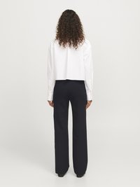 Chemise blanche courte et pantalon large bleu marine. La chemise a des manches longues et des poignets à boutons. Le tissu semble lisse et léger.