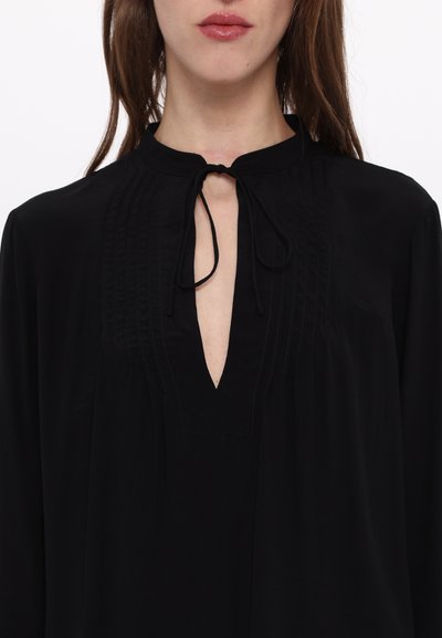 Black blouse with a high neckline, featuring a tie closure and vertical pintuck details along the front. Soft, flowy fabric.