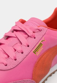 Lyserød sneaker med tekstureret stof, glatte silkesnørebånd, guld logo og orange accenter. Har en afrundet tå og en gummisål.