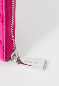Zippered wallet in vibrant pink textured material with silver-tone hardware, featuring a metal tag engraved with "MICHAEL KORS."