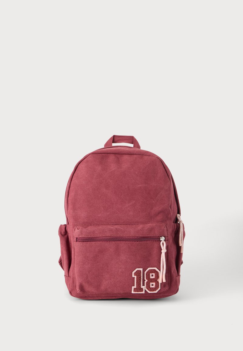 Sac à dos en tissu rouge avec poche zippée à l'avant, poches latérales, poignée supérieure et écusson numéro 18 dans le coin inférieur avant.