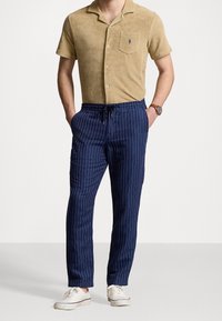 Kortärmad beige frottétröja med ficka, kombinerad med marinblå randiga byxor med dragsko; avslutad med vita sneakers.