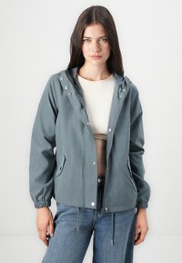 Vindjakke i dempet blågrå farge, med hette, knapper med trykknapp, elastiske mansjetter og frontlommer, laget av lett stoff.