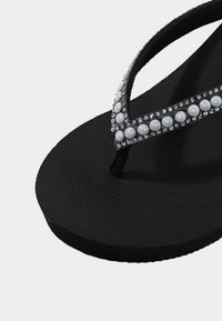 Black flip-flop with textured sole, featuring a thong strap embellished with white faux pearls and clear rhinestones.