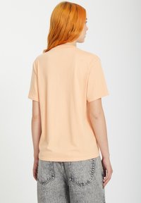 T-shirt en coton pêche à manches courtes, col rond et coupe décontractée, associé à un pantalon en denim gris clair avec poches arrière.