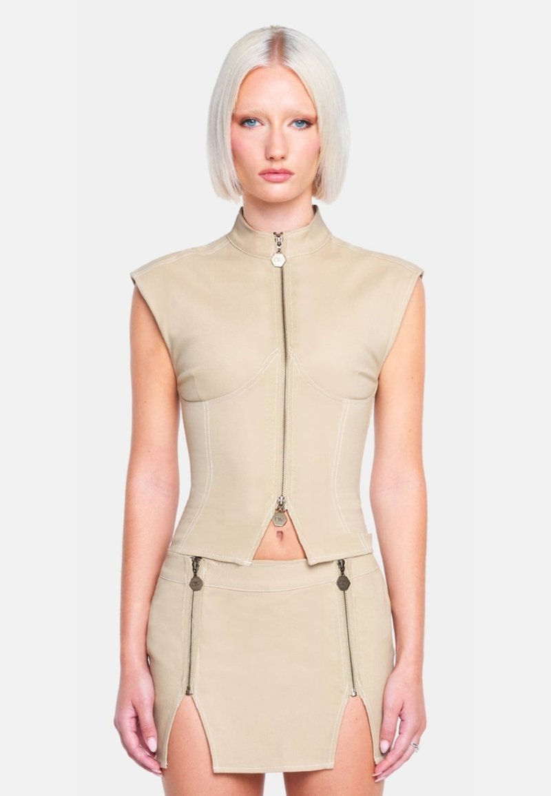 Beige verkürzte Weste mit hohem Kragen und Reißverschluss vorne, kombiniert mit einem passenden Minirock mit Seitens Reißverschlüssen und Schlitzen. Glatte Textur.