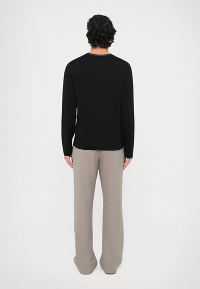 Czarny sweter z prążkowanym dekoltem i długimi rękawami, połączony z jasnoszarymi spodniami o szerokich nogawkach. Gładka faktura, minimalistyczny design.