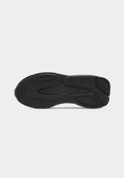 Semelle de chaussure noire avec motifs de bande de roulement texturés et logo "HUGO" embossé près du talon, présentée sur un fond blanc uni.