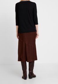 Haut noir à manches trois quarts associé à une jupe midi marron avec un motif texturé et un détail de couture diagonale, complété par des bottes marron hauteur genou.