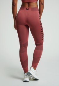 Hoge taille legging in donkerroze met een getextureerd chevronpatroon en zijkanten, gecombineerd met witte sportschoenen.