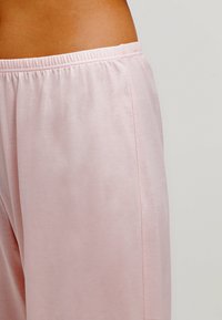 Pantalones de ocio rosa claro con cinturilla elástica, tejido suave y textura lisa. Presentan una costura lateral a lo largo de la longitud de los pantalones.