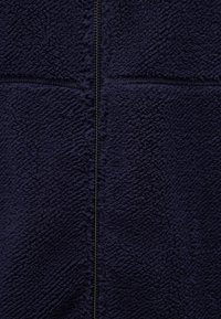 Giacca in pile navy con una superficie morbida e texturizzata. Presenta una chiusura centrale con zip e un design a pannelli. Adatta per mantenere il calore e per l'abbigliamento casual.