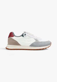 Zapatilla blanca con paneles de ante gris, beige y rojo, un diseño de calavera y huesos en el lateral, y una suela de goma marrón.