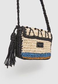 Splotkowana torba w odcieniach beżu, niebieskiego i czarnego z plecionym paskiem i detalem w postaci frędzli. Posiada plakietkę z logo oraz dekoracyjne czarne koraliki.