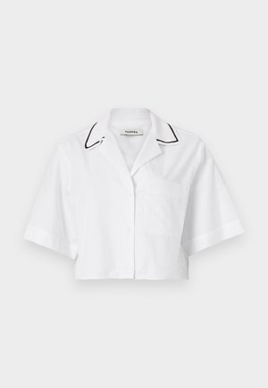 Witte verkorte shirt met korte mouwen, knoopsluiting, borstzak en zwarte piping langs de kraag. Gemaakt van lichte, ademende stof.