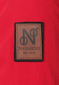 Rode stof met een rechthoekige leren label. Het label toont het "NAVAHOO"-logo, omringd door een zwarte rand, met "EST 2014" eronder.